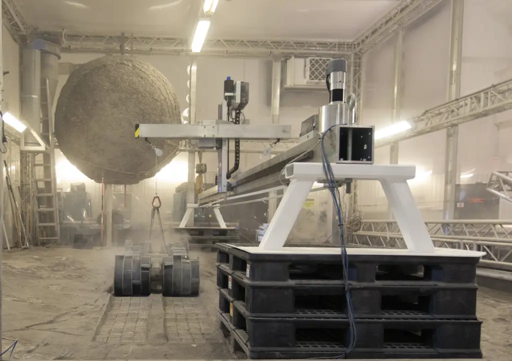 Engine plumes are being fired into a roughly 6.5‑foot‑wide, 1‑foot‑deep bin of lunar regolith simulant to observe cratering and ejecta under vacuum.